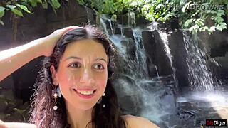 in the public locker room, she gets cum on her face, then walks to the waterfall with it