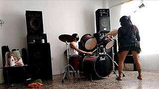 They play the drums for her. She dances stripping and showing her ass.