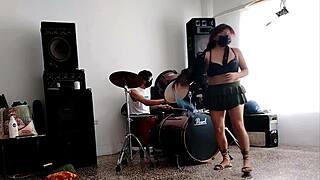 They play the drums for her. She dances stripping and showing her ass.